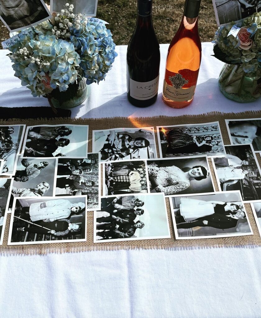 Memorial table covered in black and white photos alongside wine bottles and floral arrangement