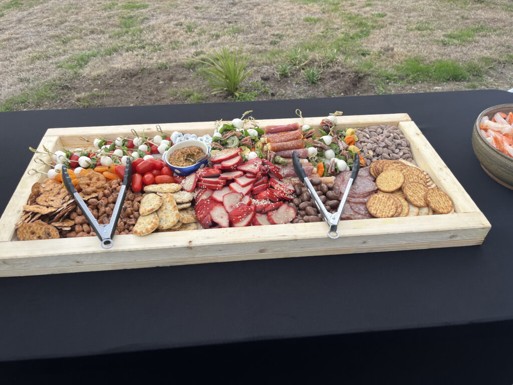 Curated grazing board with charcuterie, crackers, and antipasti on a black tablecloth