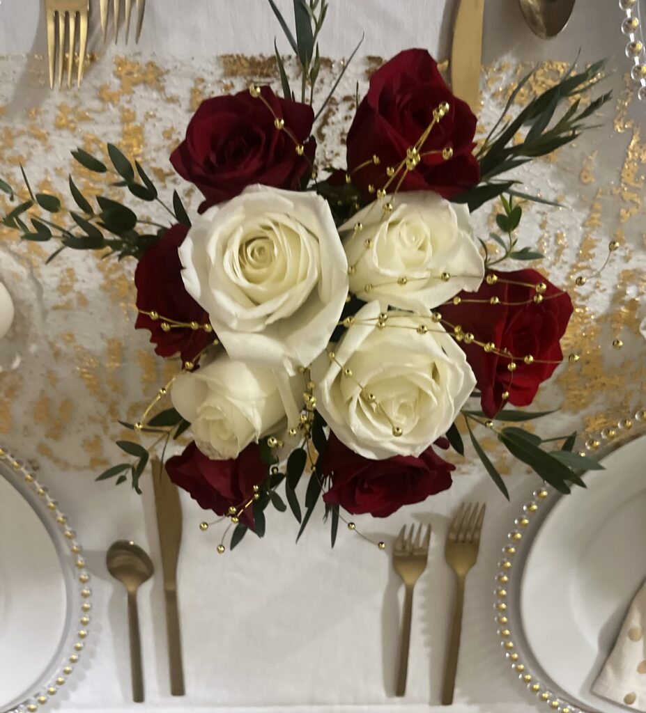 Overhead view of red and white rose centrepiece with gold cutlery on a formal table