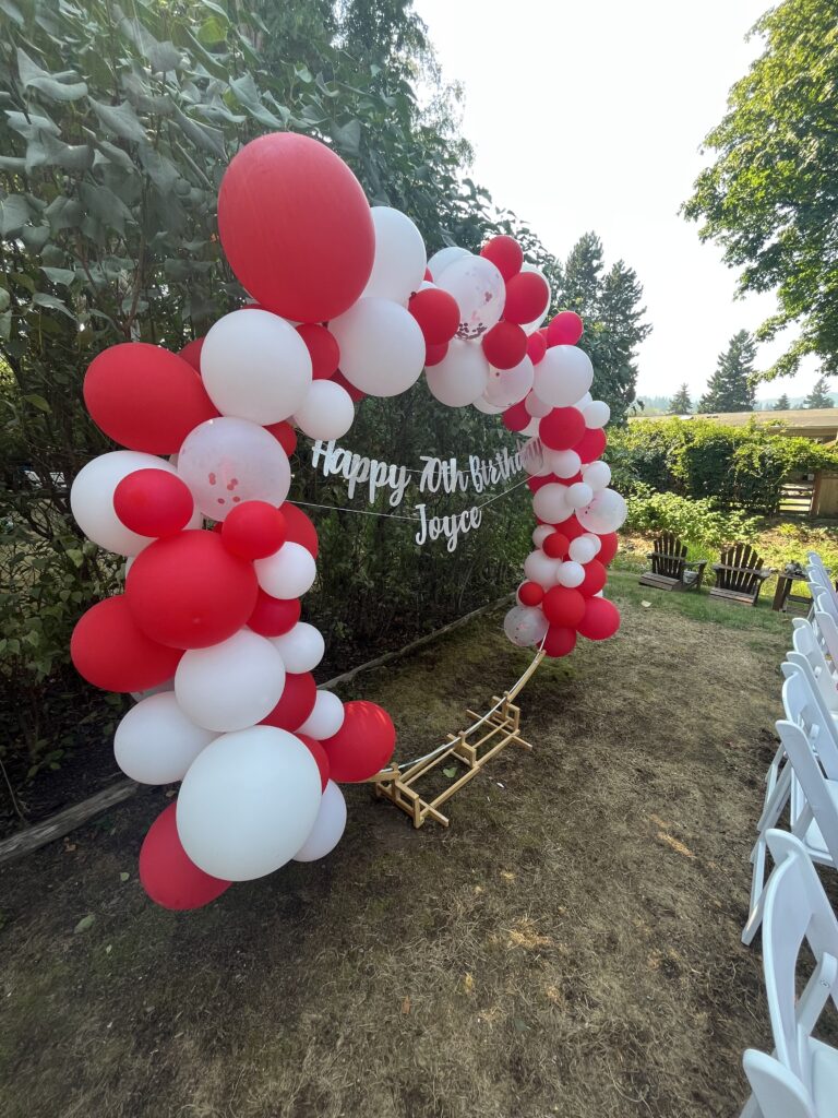 Large red and white balloon arch installed outdoors for a milestone birthday party