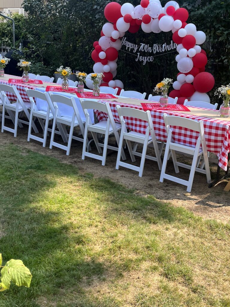 Outdoor birthday party with long table, red gingham linens, and festive balloon arch